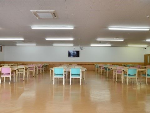 食堂には、列を整えてテーブルセットが並んでおり、清潔感がある。ピンク色またはブルーの椅子きれいに配置されている。
