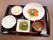 黒いお盆の上に、ご飯、汁物、キュウリの漬物、パスタサラダ、赤魚の煮つけが乗っている。主菜にはオクラとニンジンも添えられている。