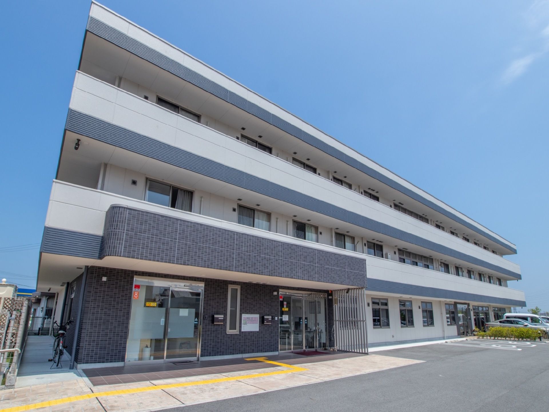 グレーを基調とした３階建ての建物である。駐車場からは出入り口までフラットなのでスムーズに出入りできる。