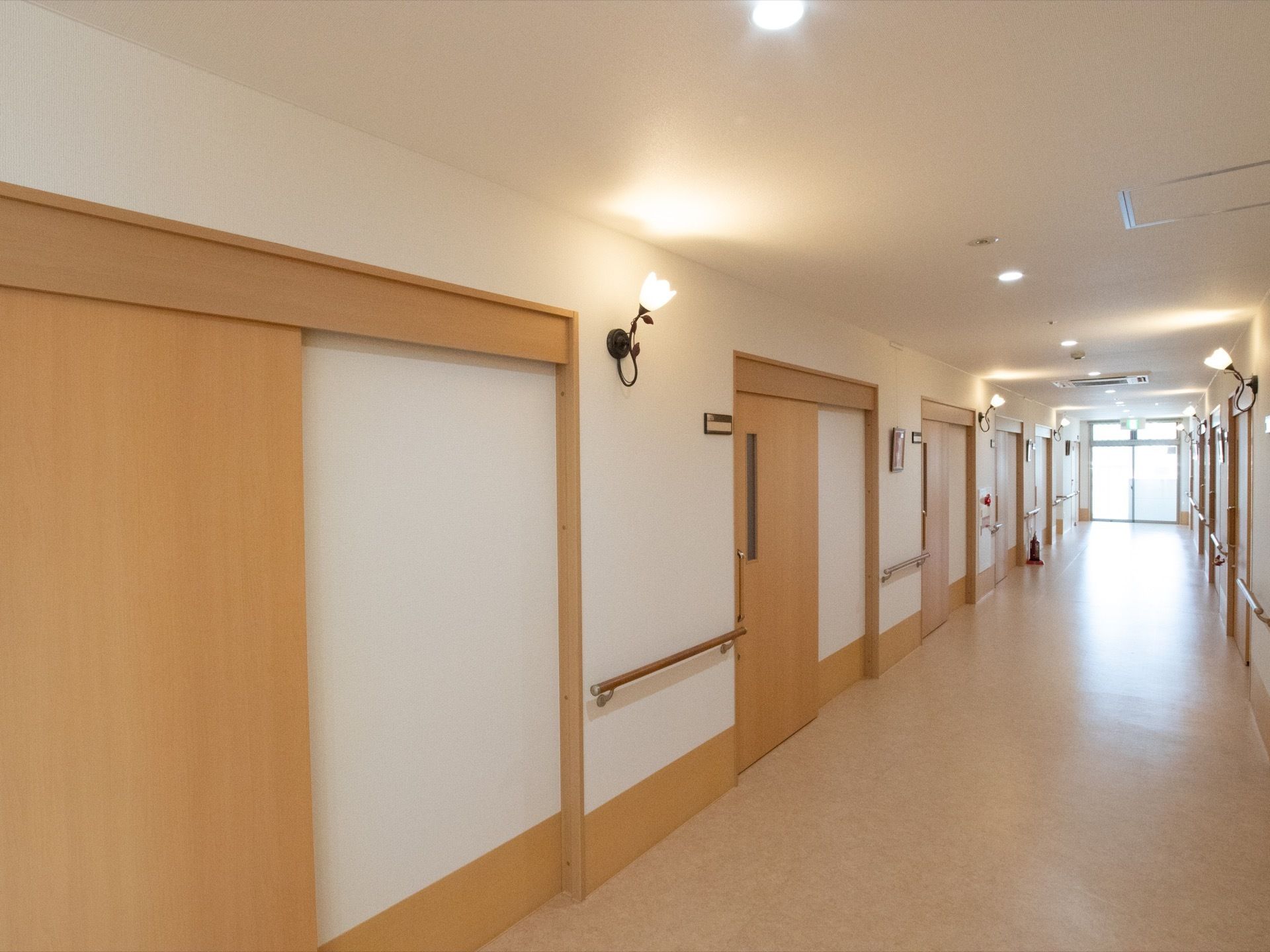 ２階通路はゆったり広々としていて、ナチュラルカラーの居室ドアが並んでいる。アンティーク風の照明がやさしく照らしている。