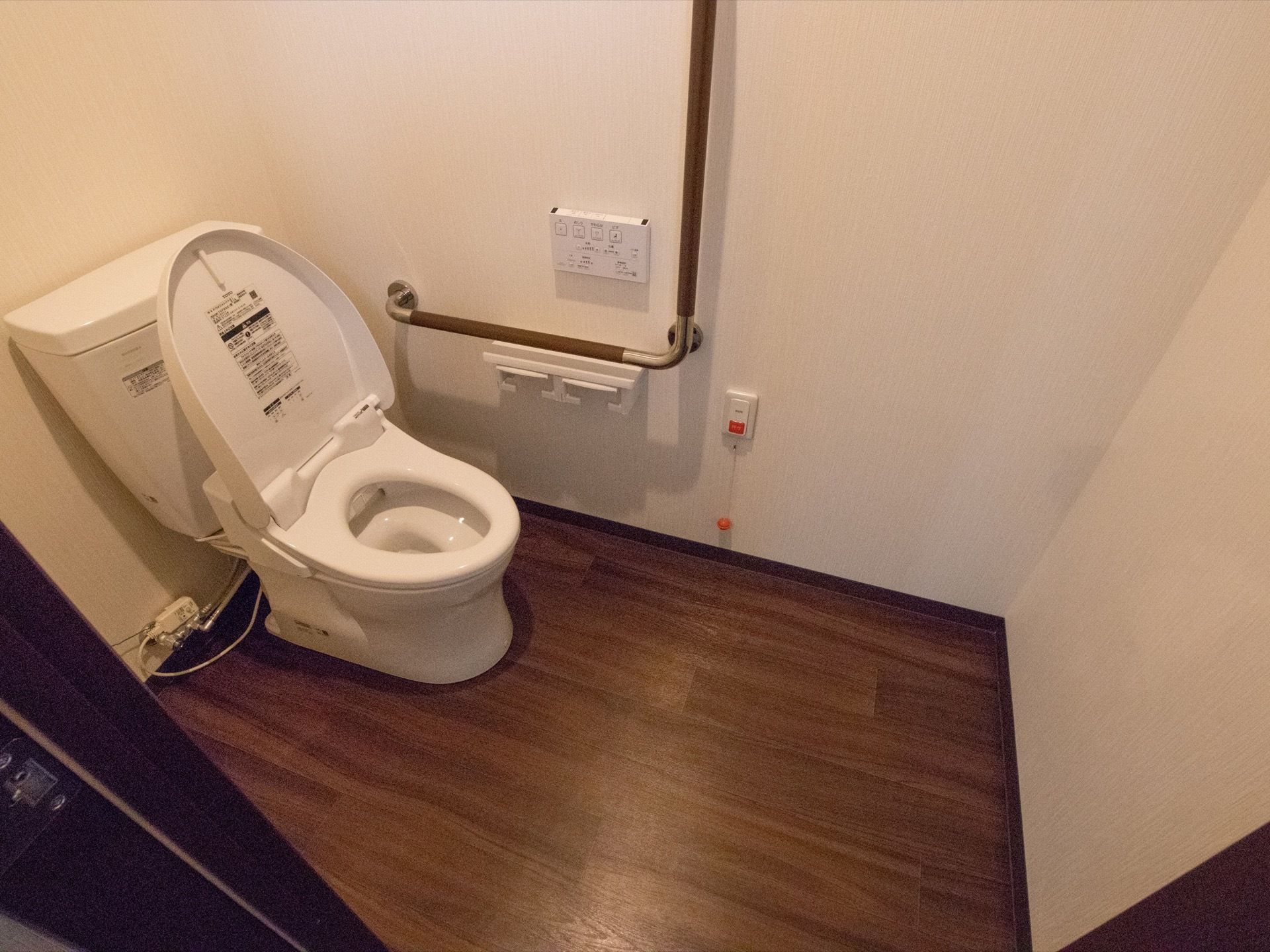 トイレにはＬ字型の手すりと緊急通報装置、２つ並んだペーパーホルダー、温水洗浄便座の操作パネルが設置されている。