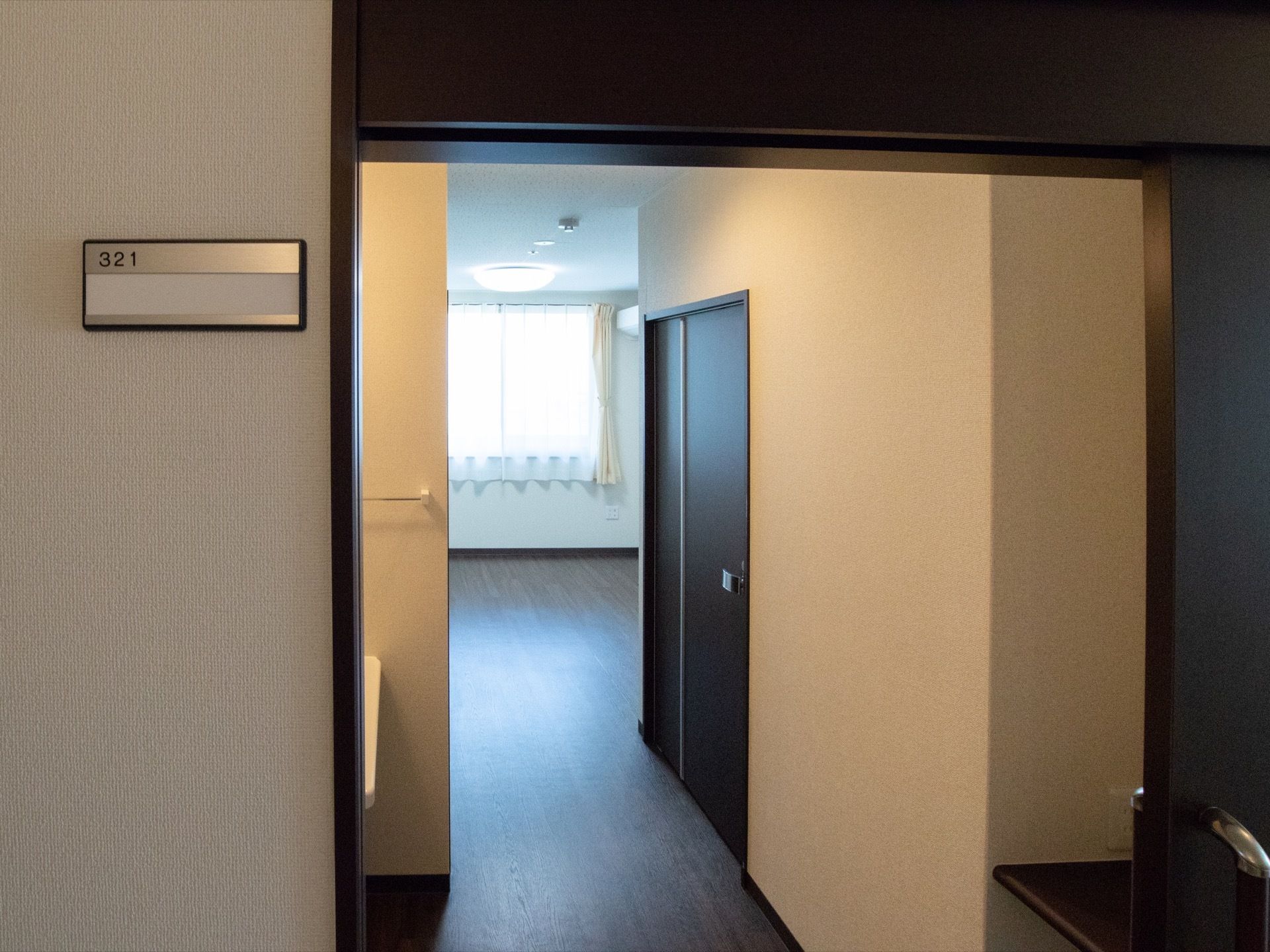 居室の入り口ドアが開いていて部屋の中が見渡せる。入り口の横には部屋番号の書かれたプレートがあり、通常のマンションのような雰囲気である。