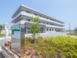 広々とした敷地に、重量鉄骨造の３階建ての施設が建っている。手前の植栽付近に、クリニックの看板が見える。