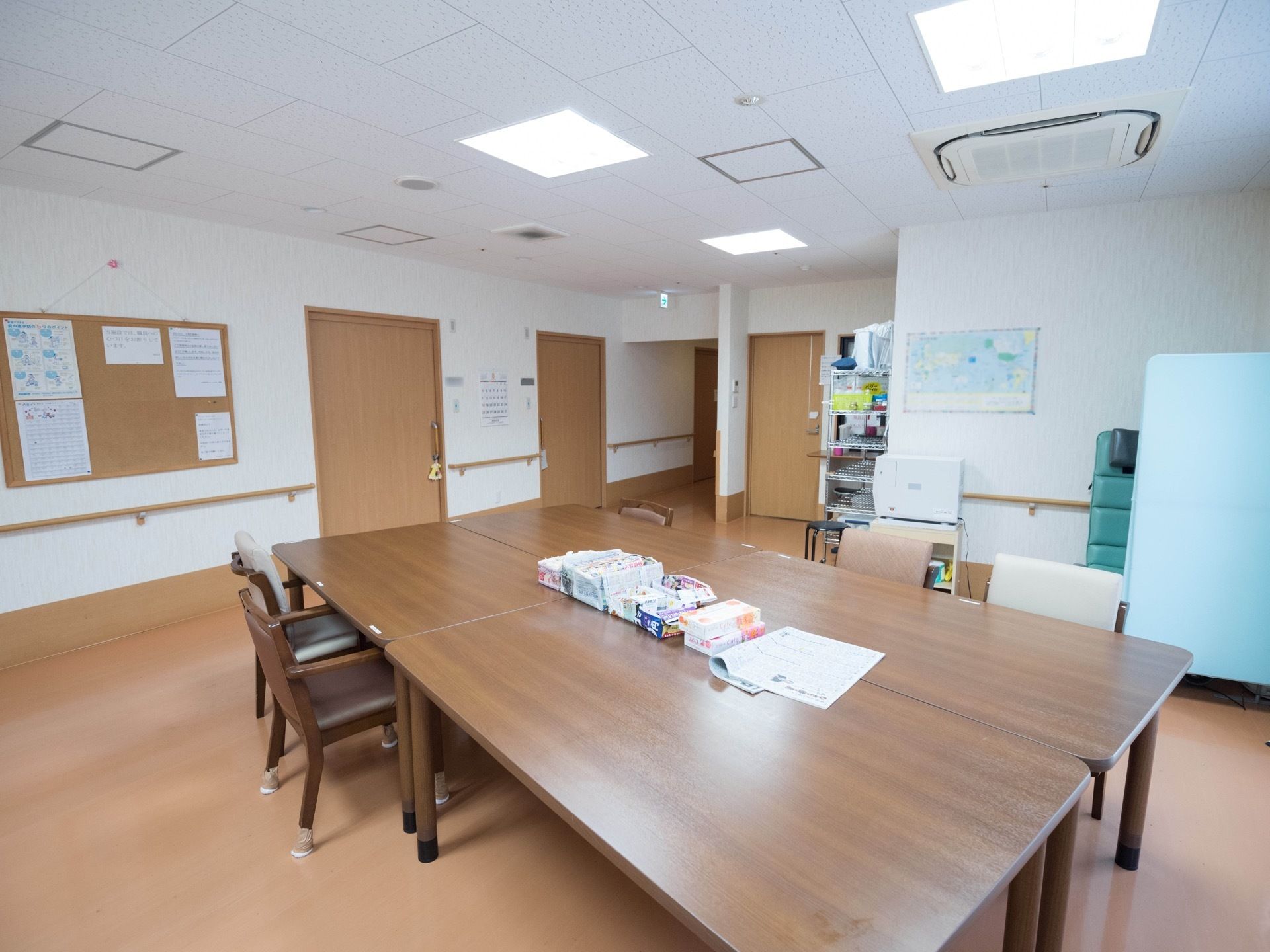 空調の付いた広いフロアがあり、ダイニングテーブルが４つ、集まるように配置されている。テーブルの上には新聞や箱ティッシュが置かれている。