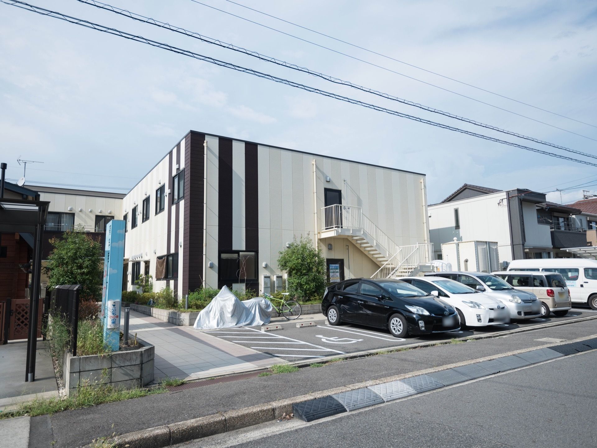 白と黒のストライプ柄が印象的な２階建ての住宅がある。建物の前は駐車場になっていて、車が５台停められている。