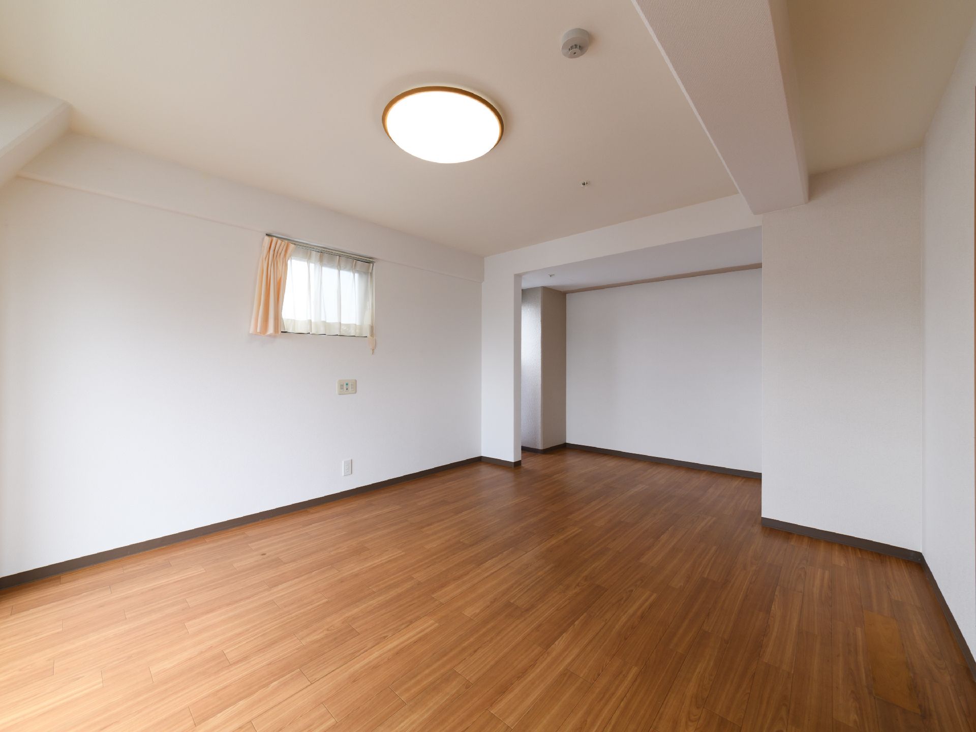 居室の床はフローリングで広く、白い壁なのですっきりした部屋の印象である。小さな窓があり、レースのカーテンがついている。