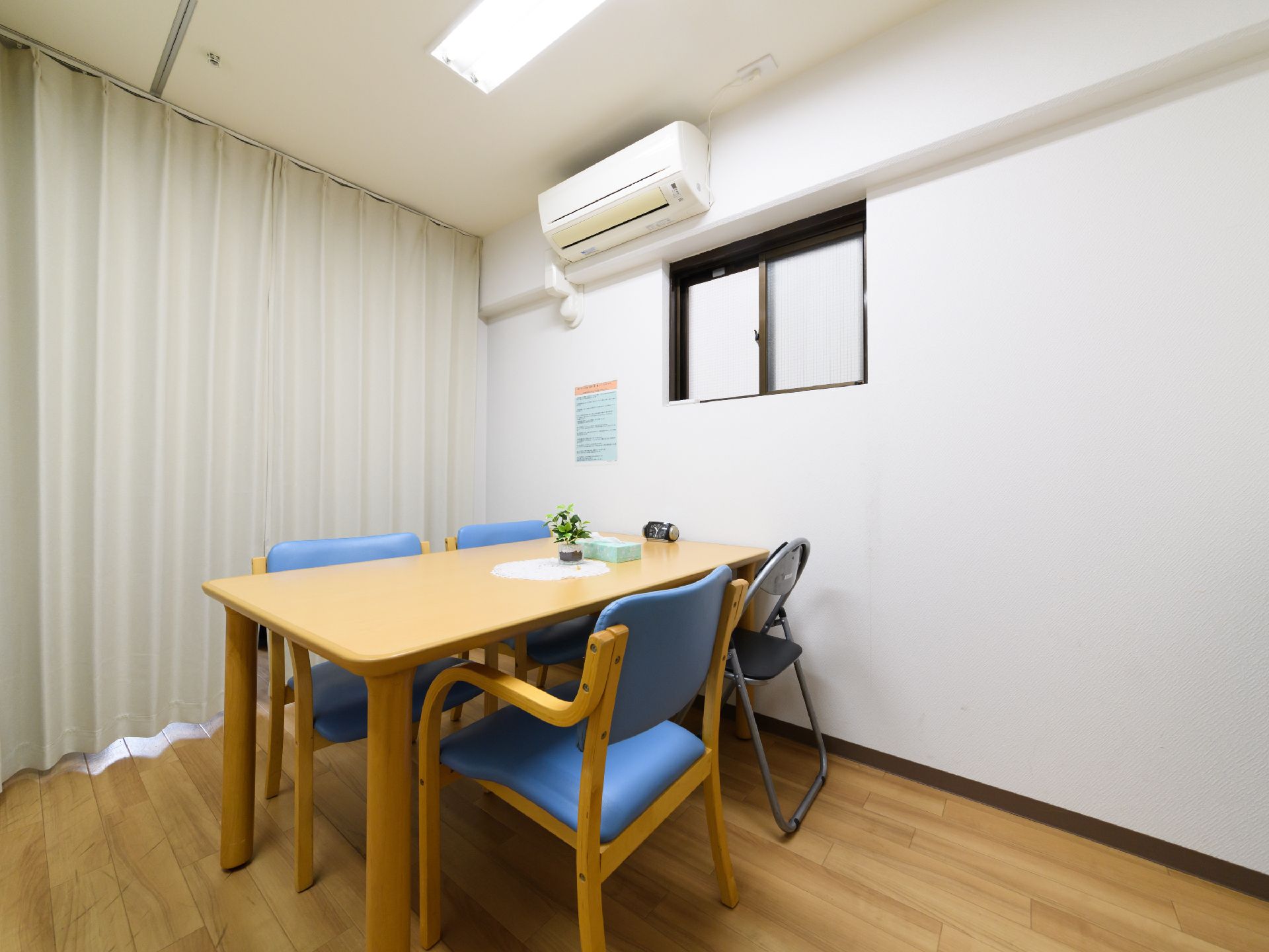 談話室には、4人掛けテーブルと椅子が配置されており、壁にエアコンが完備されている。カーテンが掛けられた大きな窓がある。