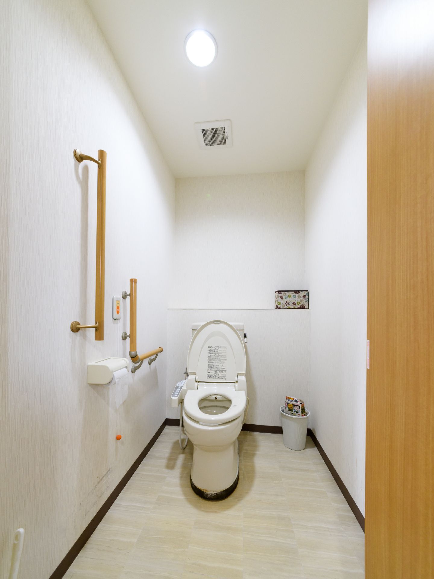 広々としたトイレである。壁には、L字型の手すりや呼び出しボタンが設置されている。ゴミ箱が置かれている。