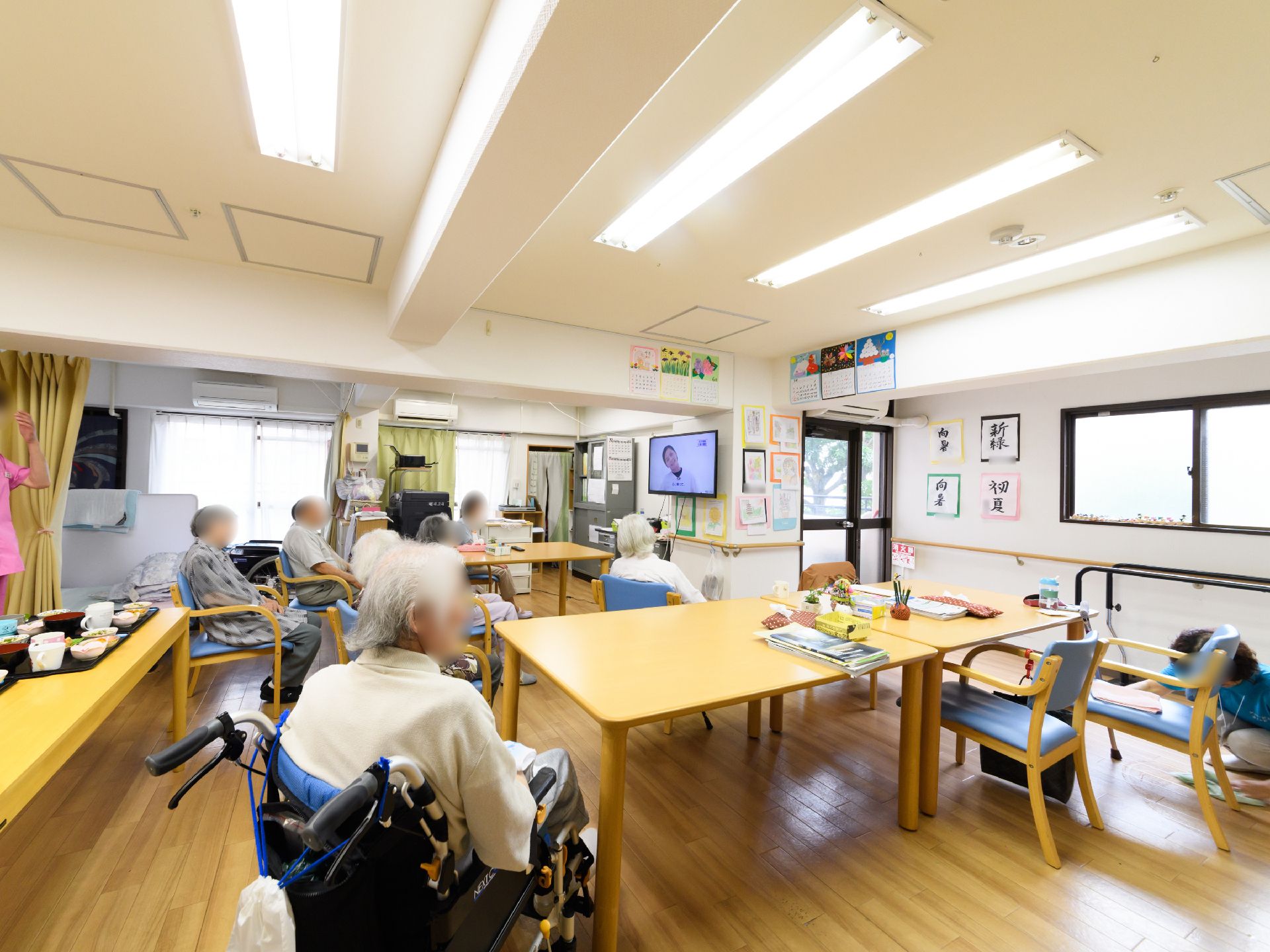 食堂にはテレビが設置されている。テレビの画面では首を曲げる体操が放送されている。画面をみながら同じ動作をする入居者様がいる。