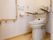 施設内のトイレである。背もたれと両脇に肘おきが取り付けられている。また壁には手すり、ナースコール、ウォシュレットの操作盤が設置されている。