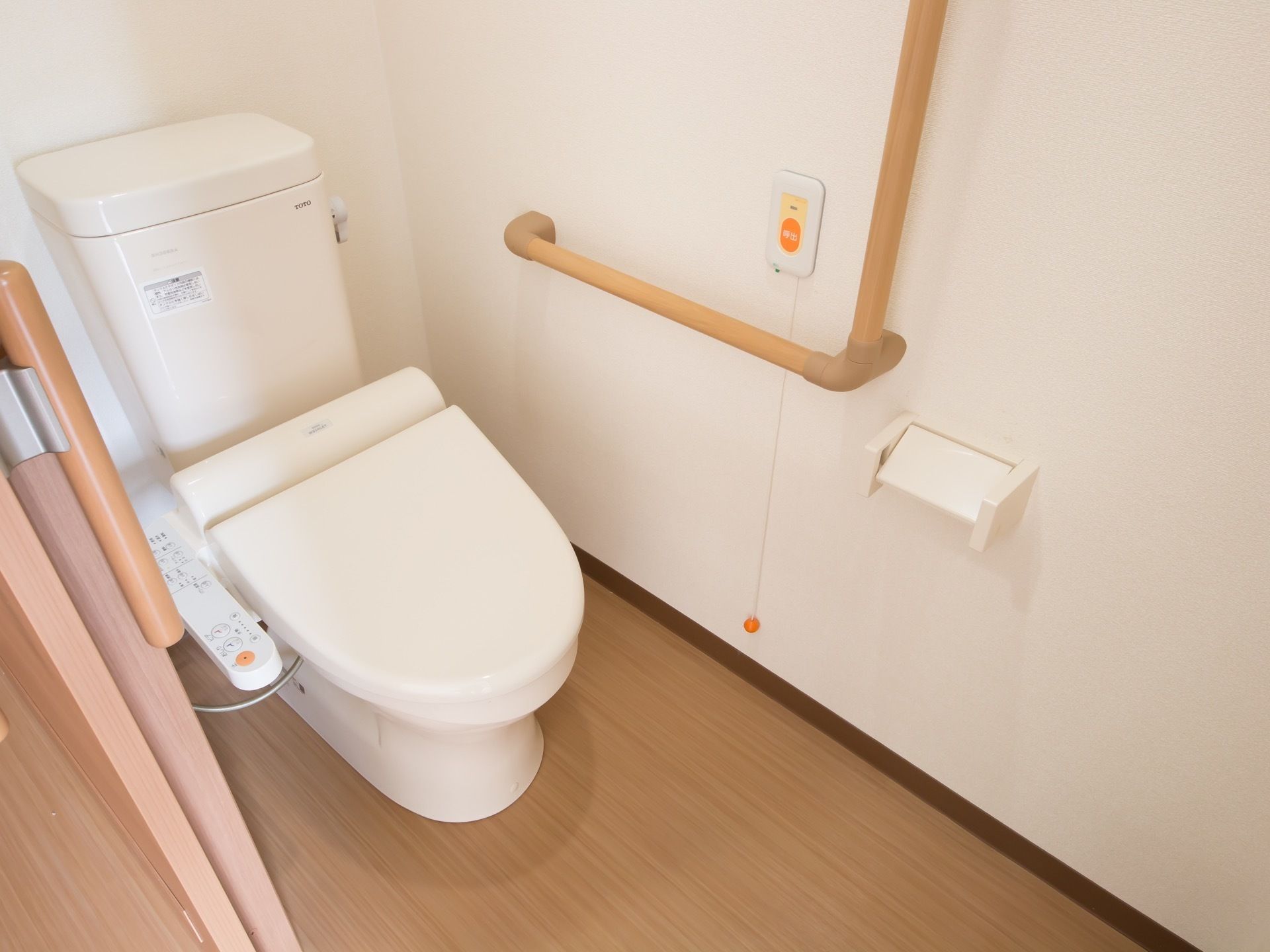 居室内に設けられているトイレ。左手側の壁にはＬ字型の手すり、そして緊急時用のナースコールが設けられている。