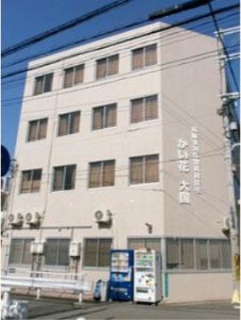 グレーの外壁と、ブラウン系のカーテンが窓にかかり、落ち着いた雰囲気の施設の外観。施設内には快適な生活のための様々なサービスを用意している。