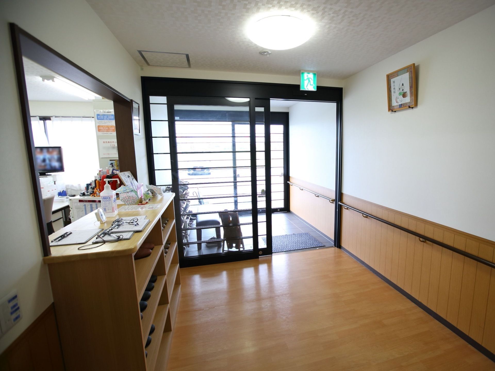 広い間口の玄関である。全面ガラスのドアで室内は明るい。風除室を入るとすぐに受付があり、カウンターの下が上履き入れとなっている。