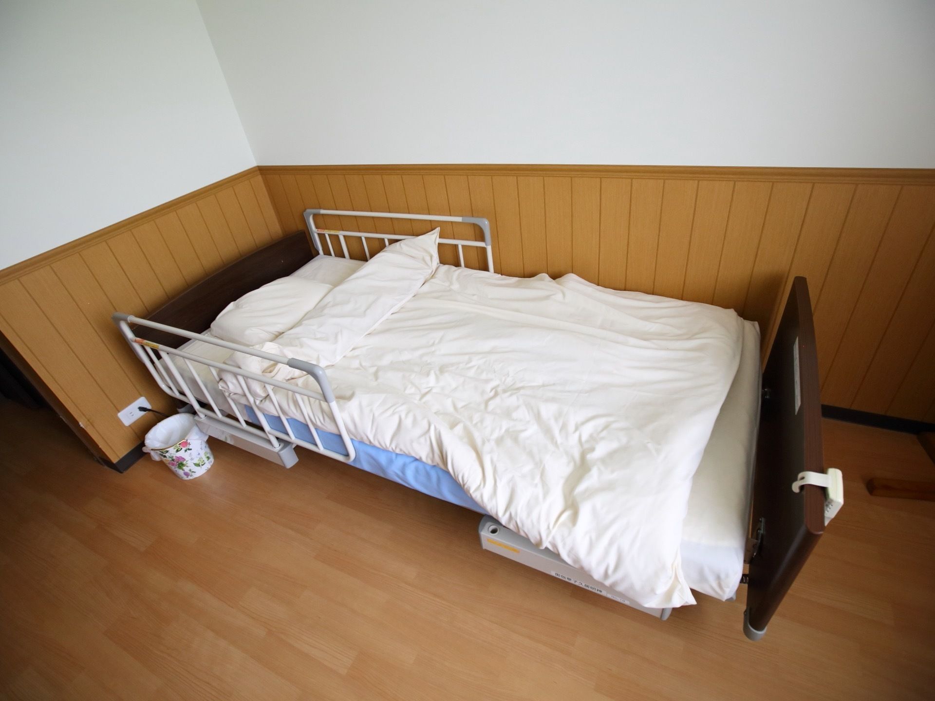 居室の床は、木目の美しいフローリングで、壁は白く、腰高の位置まで木板が貼られている。壁際にベッドが置かれ、枕元には手すりが付いている。
