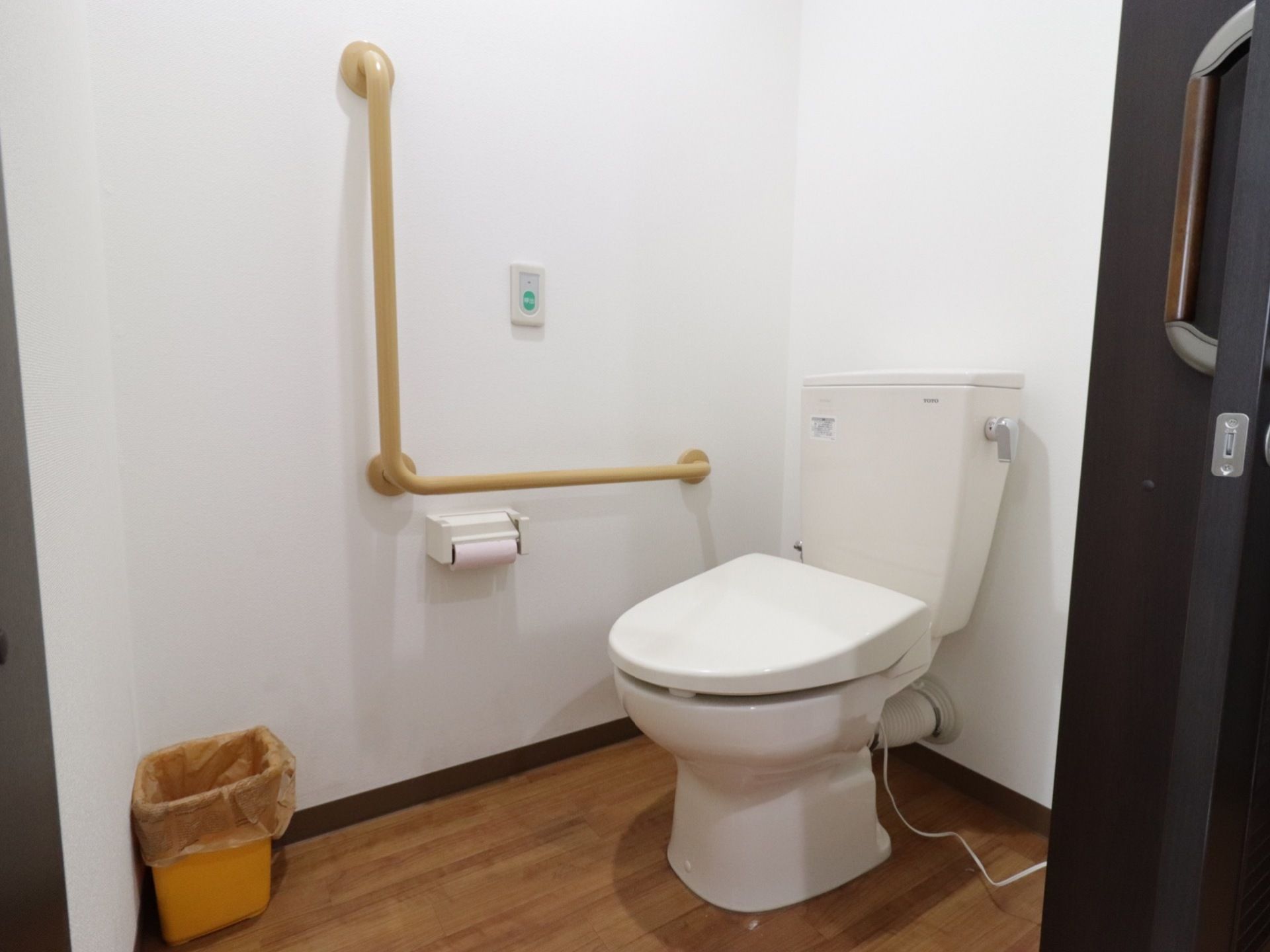 ダークブラウンのスライドドアで仕切られたトイレがある。広めの空間で、手すりがついており使いやすい設計になっている。