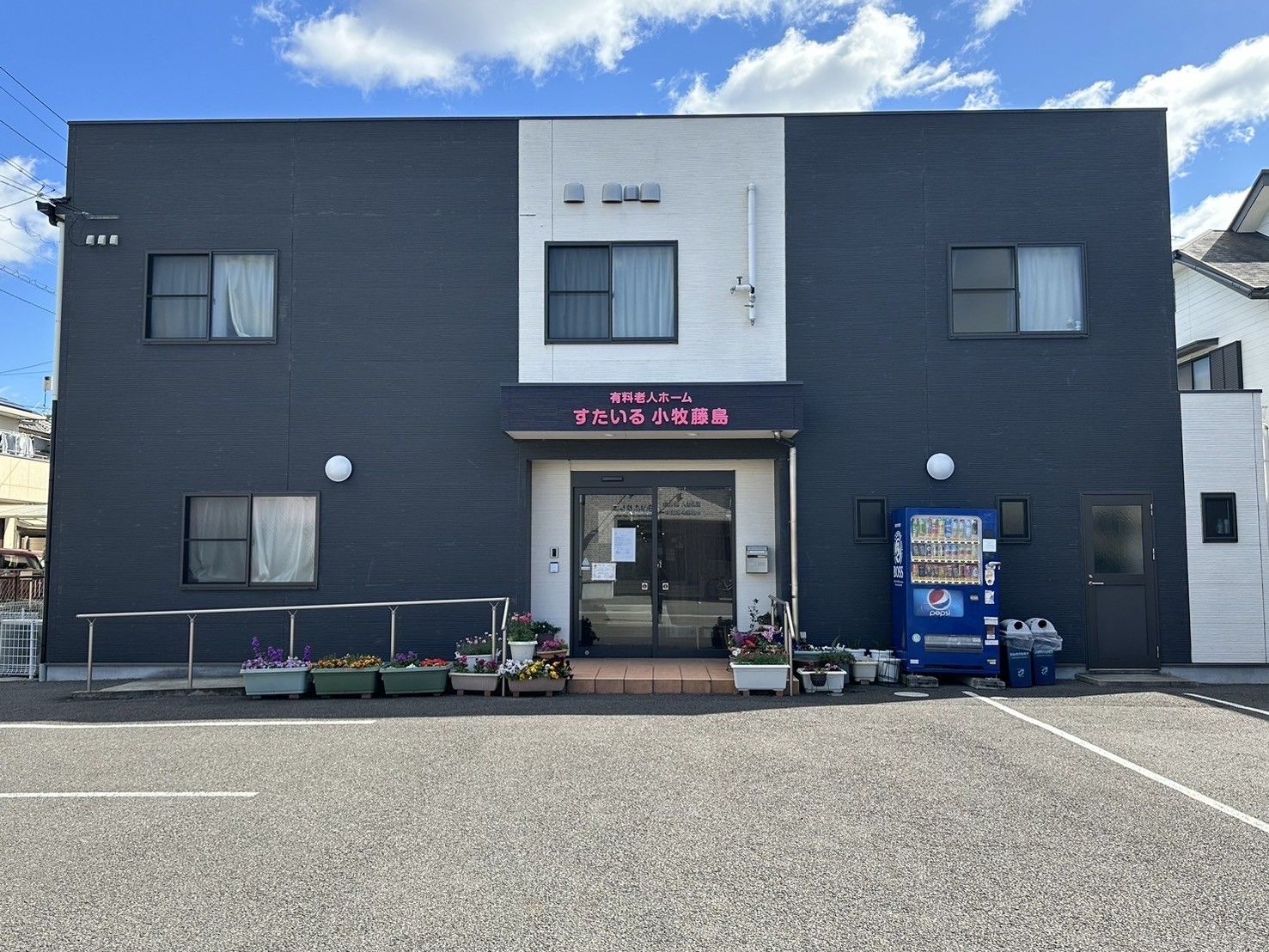 玄関ポーチは茶色いタイル敷きとなっていて、鉢植えの植物が置かれている。出入り口はガラスの自動ドアとなっている。