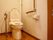 右奥にウオッシュレット式トイレがあり、右側にはアルミ製、左側には木目調のL字型の手すりが敷設されている。