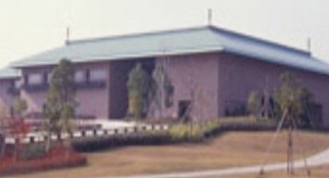 緑色の屋根とレンガのような赤い壁の平屋の建物である。入口部分が広々と開いており、そこまで道が続いている。