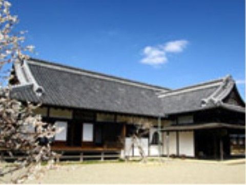 手前に桜が見える、L字型になっている平屋の建物。灰色の屋根瓦や床板の濃茶色など、いかにも歴史がありそうに感じられる。