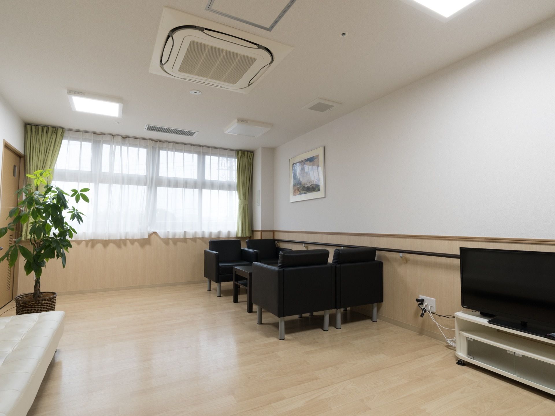 黒色のテーブルと椅子が置かれている。大型テレビがある。観葉植物が飾られている。壁には手すりが設置されている。