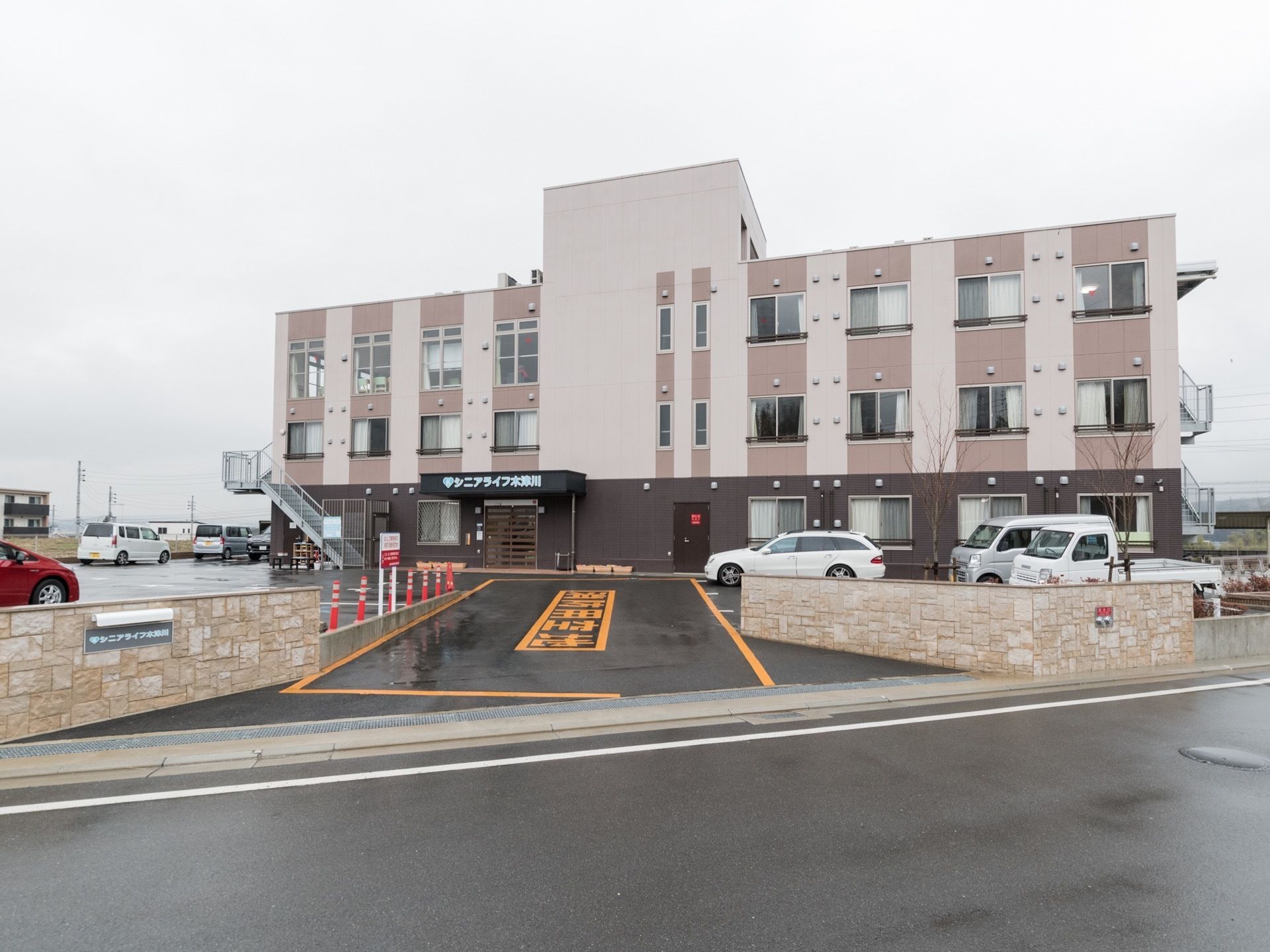3階建ての施設で、建物前に駐車場がある。茶色をベースにした建物外観で落ち着いた雰囲気である。建物に施設名が書かれている。