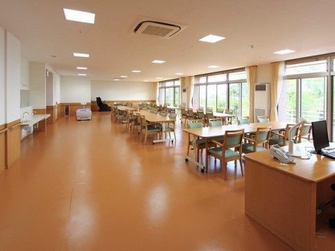 広いスペースには木製のテーブル、手すり付きの椅子が置かれている。ガラス引き戸が設けられ、壁には手すりが設置されている。