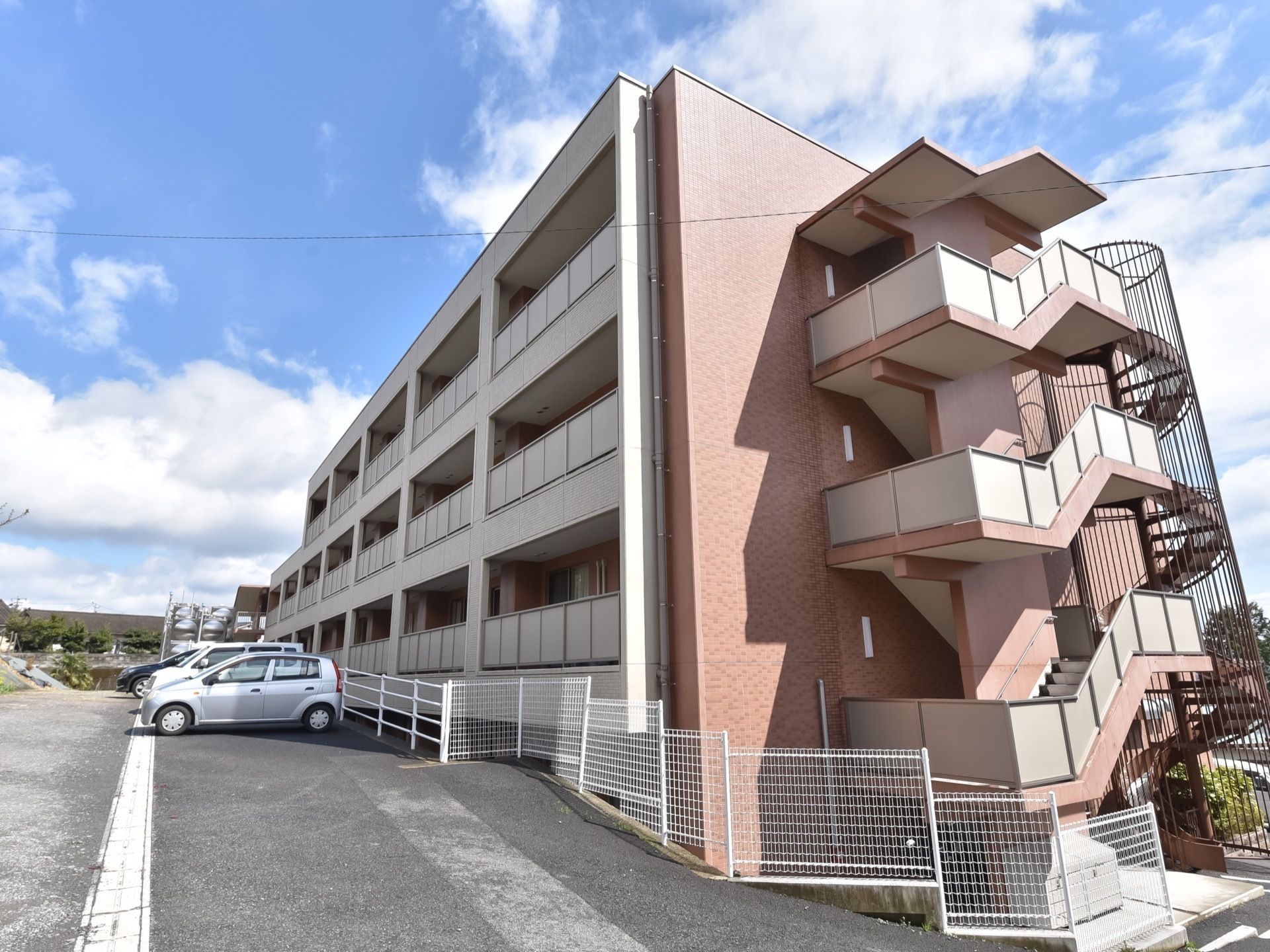 ４階建ての施設である。自動車が複数停まっている。建物の一部にフェンスが取り付けられている。居室にはそれぞれベランダがある。