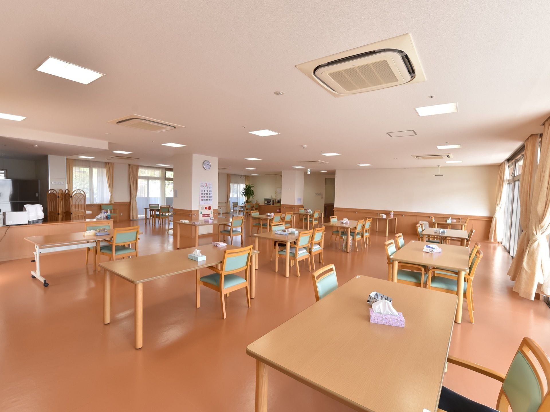 複数のテーブルと椅子が置かれている。エアコンが天井に複数設置されている。テーブルの上にはティッシュが置いてある。