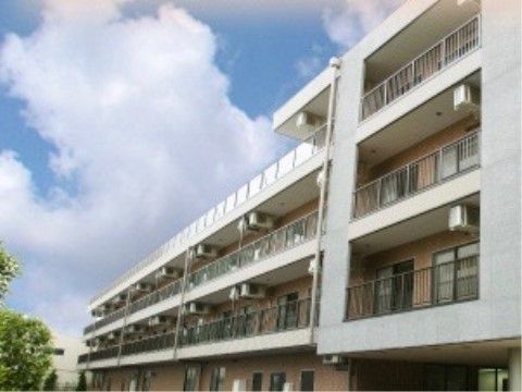 すぐ近くに背の高い木々が生えている、４階建ての施設外観