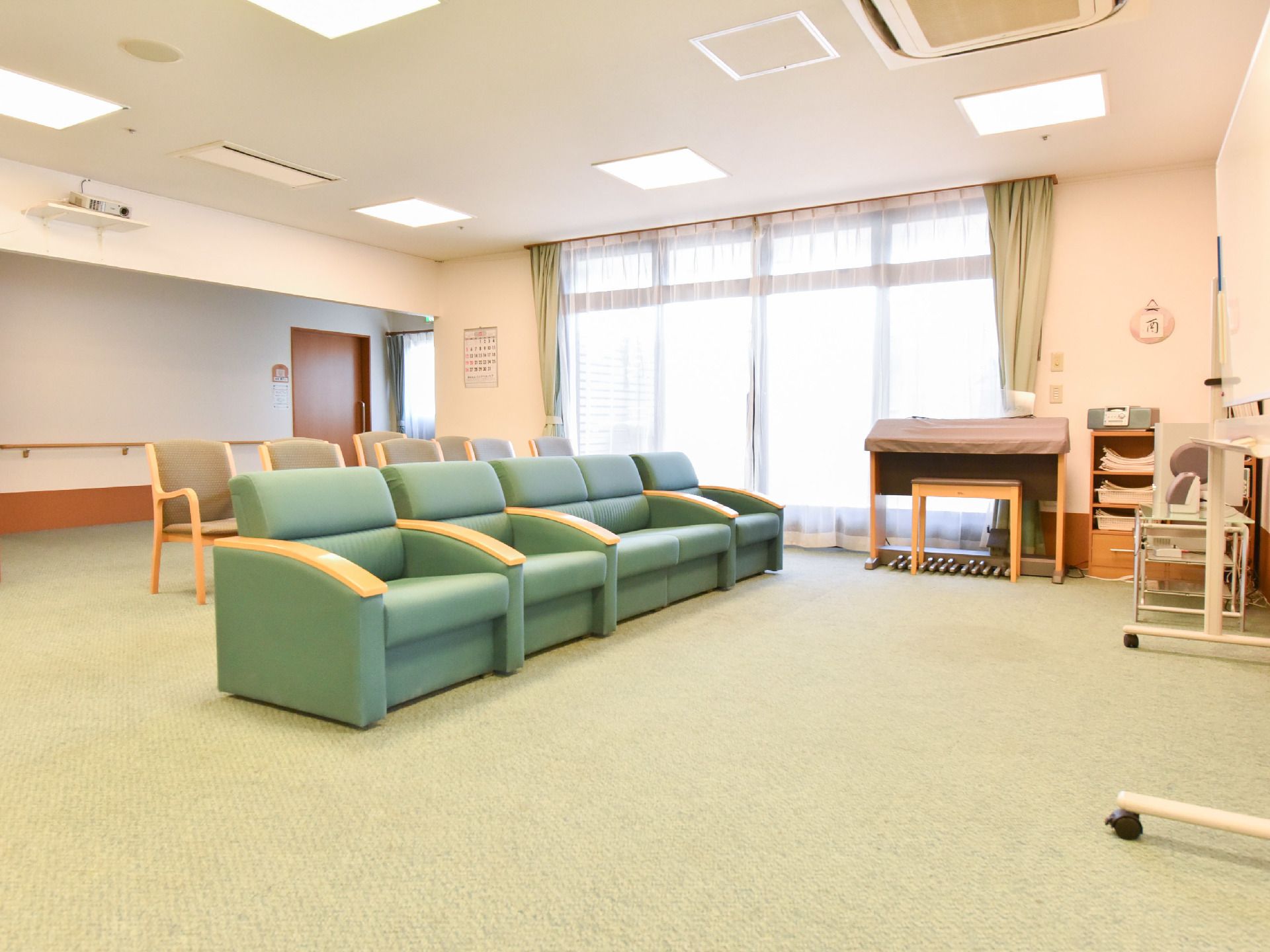 大きな窓から明るい光が部屋に差し込んでおり数台のソファと椅子が同じ方向に並べられている。カーペットは薄緑色をしている。