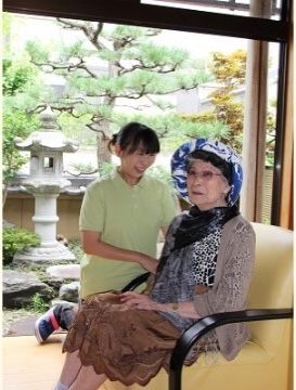 ソファチェアに座っている女性入居者様に微笑みかけている女性スタッフ