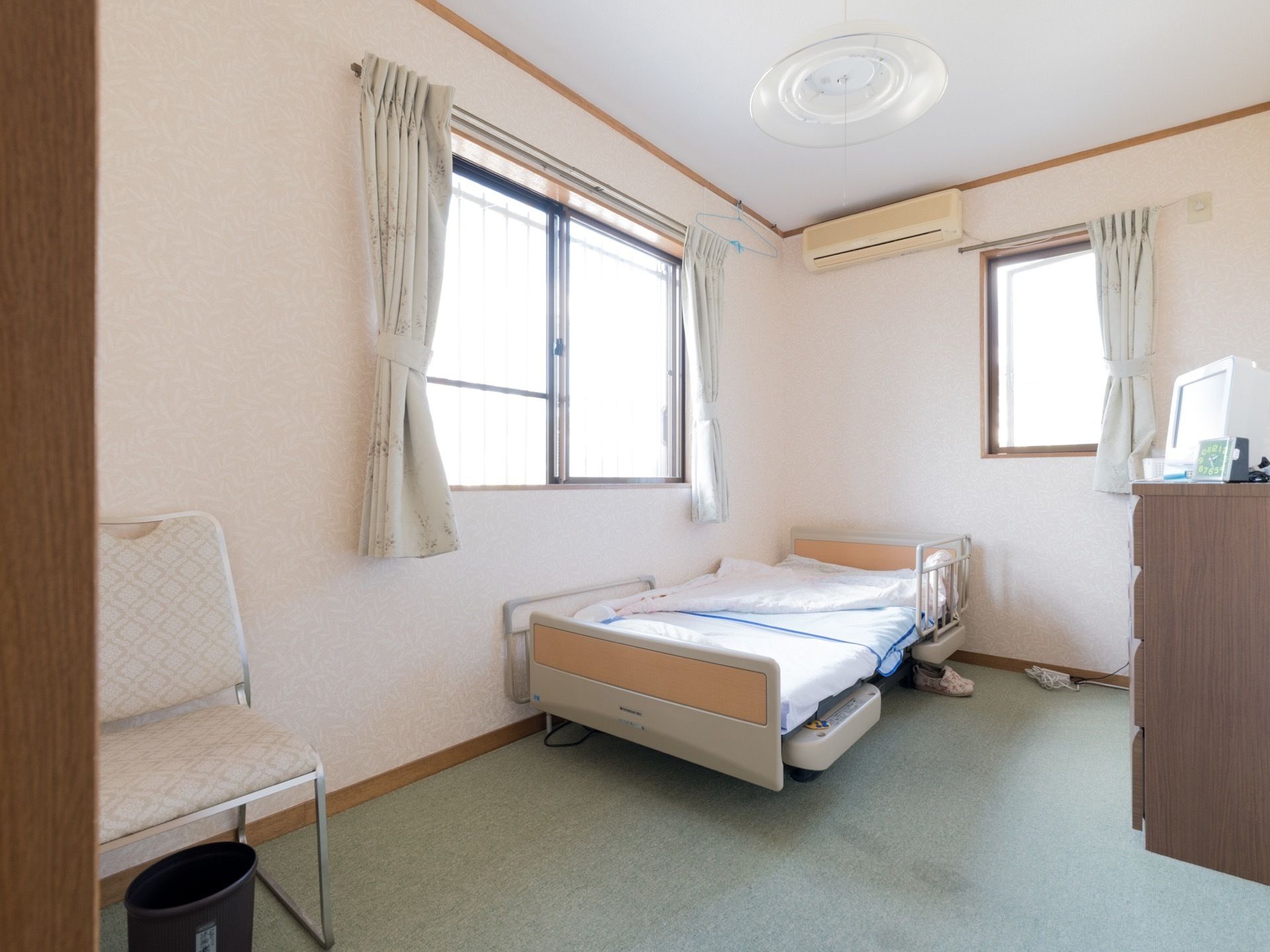 居室には窓が2つ設置されている。ベッドには手すりが取り付けられている。近くには背もたれ付きの椅子も置かれている。