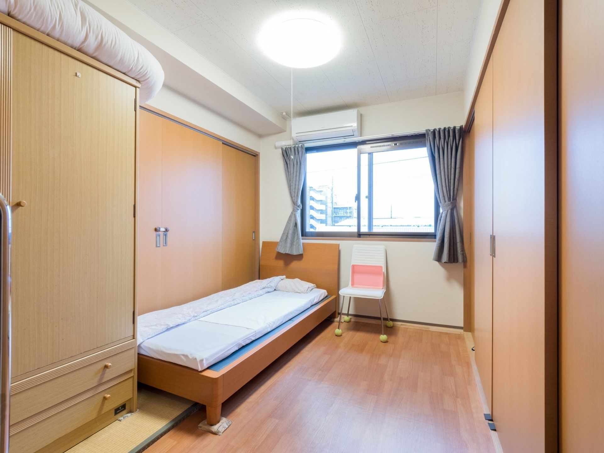 居室にはカーテンを掛けた窓があり、上部にエアコンを設置している。左側にはクローゼットとベッドを配置している。