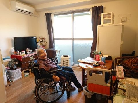 居室の中央部で、車いすに座って微笑んでいる女性の入居者様