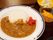 大皿にご飯とカレーが盛り付けてあり、右端に色鮮やかな福神漬が添えてある。その横には、ガラスの器に入ったミカンが見える。
