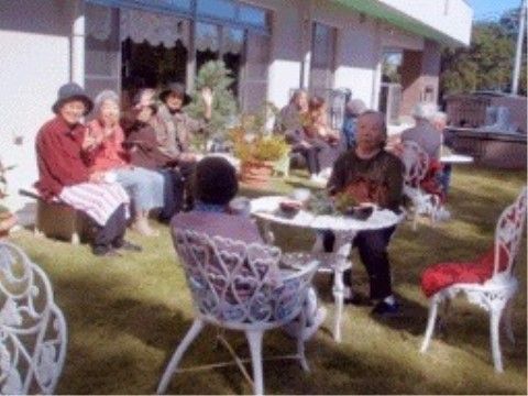 芝生の上に置かれたガーデンチェアやベンチに添わってにこやかな表情をしている女性入居者様たち