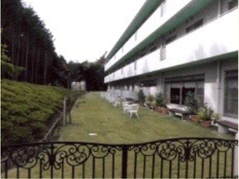 手前に門がある。手入れの行き届いた芝生の上に椅子が置かれている。施設１階の窓からガーデンに出たところにはベンチが用意されている。
