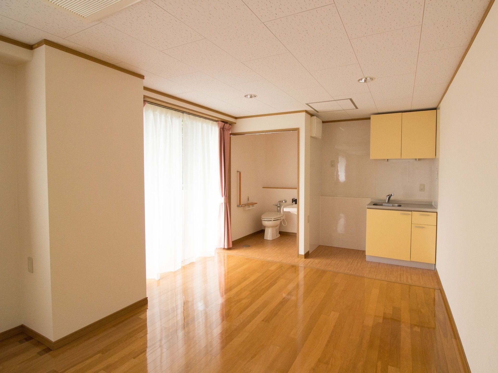 部屋はフローリングでできており、簡易キッチンと、トイレが備えつけられている。広くて開放的な空間になっており、窓も大きく陽射しも入る。