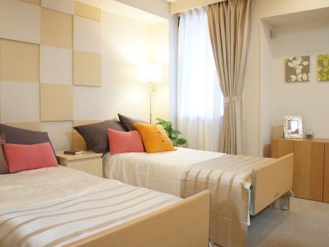 ベッドが２つ並んでいる。白と黄色のタイルのような柄の壁が明るい雰囲気を演出している。壁際の棚には写真立てが飾られている。