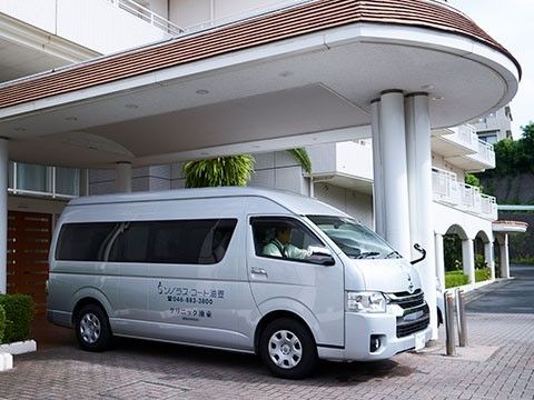 玄関の前に施設の送迎用の車が止まっている。玄関の前には雨よけがあるため、雨に濡れずに出入り可能である。