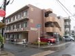 施設の建物は落ち着いた色の３階建て。建物の正面右側には１階から３階までつながっている外階段がついている。
