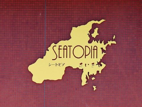 落ち着いた赤色の壁に、黄色い看板がある。施設名等の文字は、地図を形取った看板を切り抜いて表している。