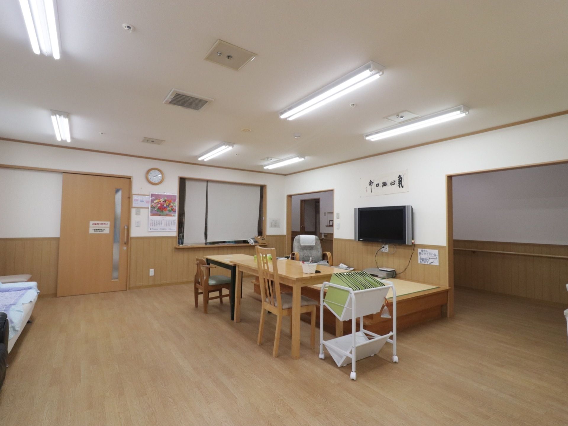 廊下と食堂を区切るドアがない。壁にはテレビが設置され、その下に畳のスペースがある。椅子とテーブルもある。