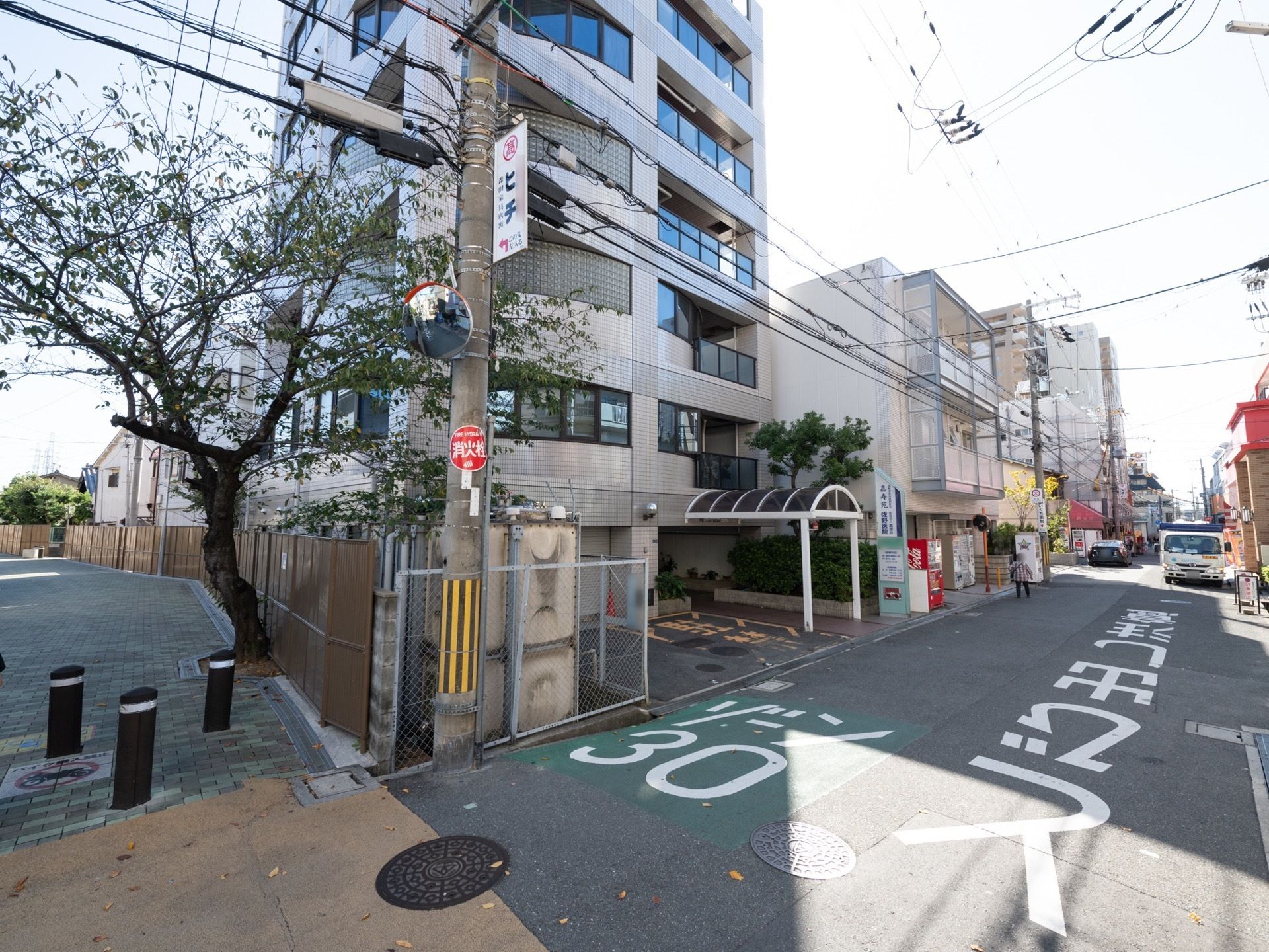 施設の前は商店街になっている。横は遊歩道があり、大きな木が生えている。建物からはアーチ状の屋根が出ている。