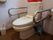 便器の両サイドに可動式手すりが設置されたトイレである。洗面台が完備されている。トレイブラシとラバーカップが置かれている。