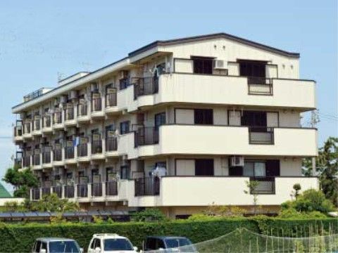 マンションのような佇まいをしている。建物の周りには手入れをされた植木がある。車を停めるスペースも用意されている。