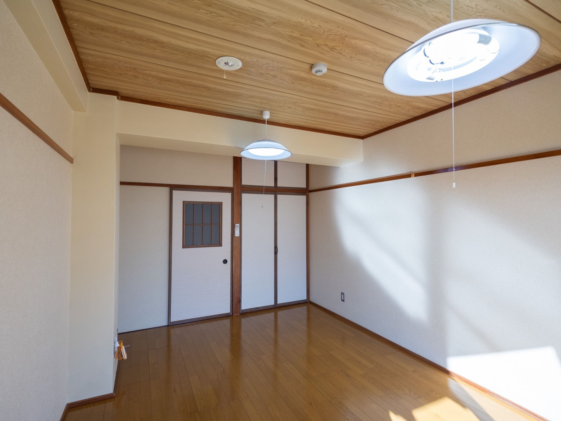 天井の板目と照明の笠から和式を感じる居室である。床はフローリングとなっている。入口ドアは引き戸式である。