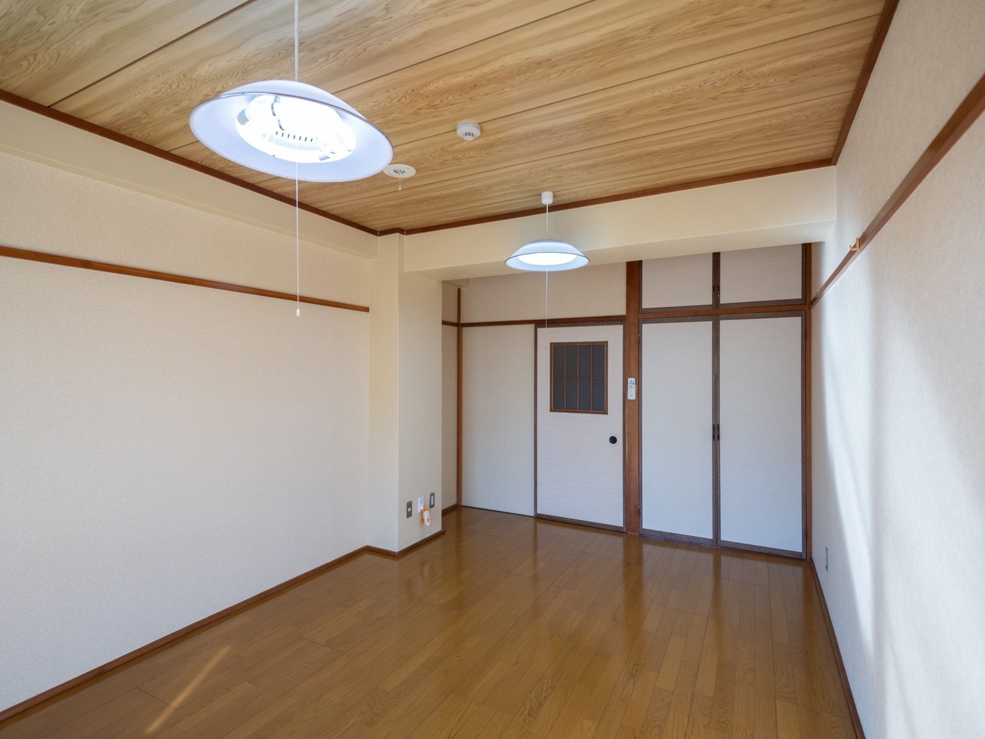 天井の板目がきれいな日本間の居室である。丸い和風の照明が下がっている。横には、火災感知器が設置されている。