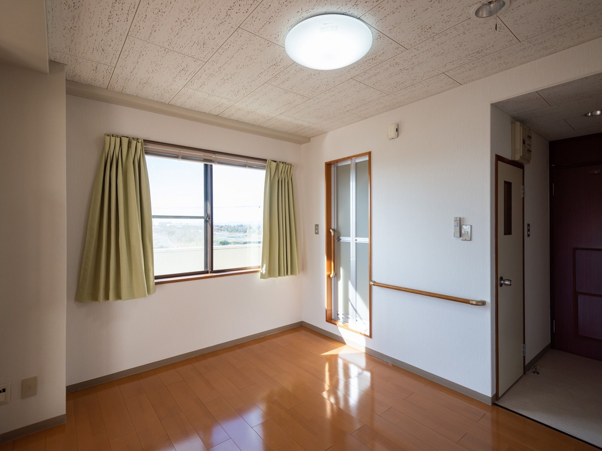洋間の居室である。丸い天井照明が付いている。フローリングの床に、高窓からの陽光が反射している。窓からは外の景色が望める。