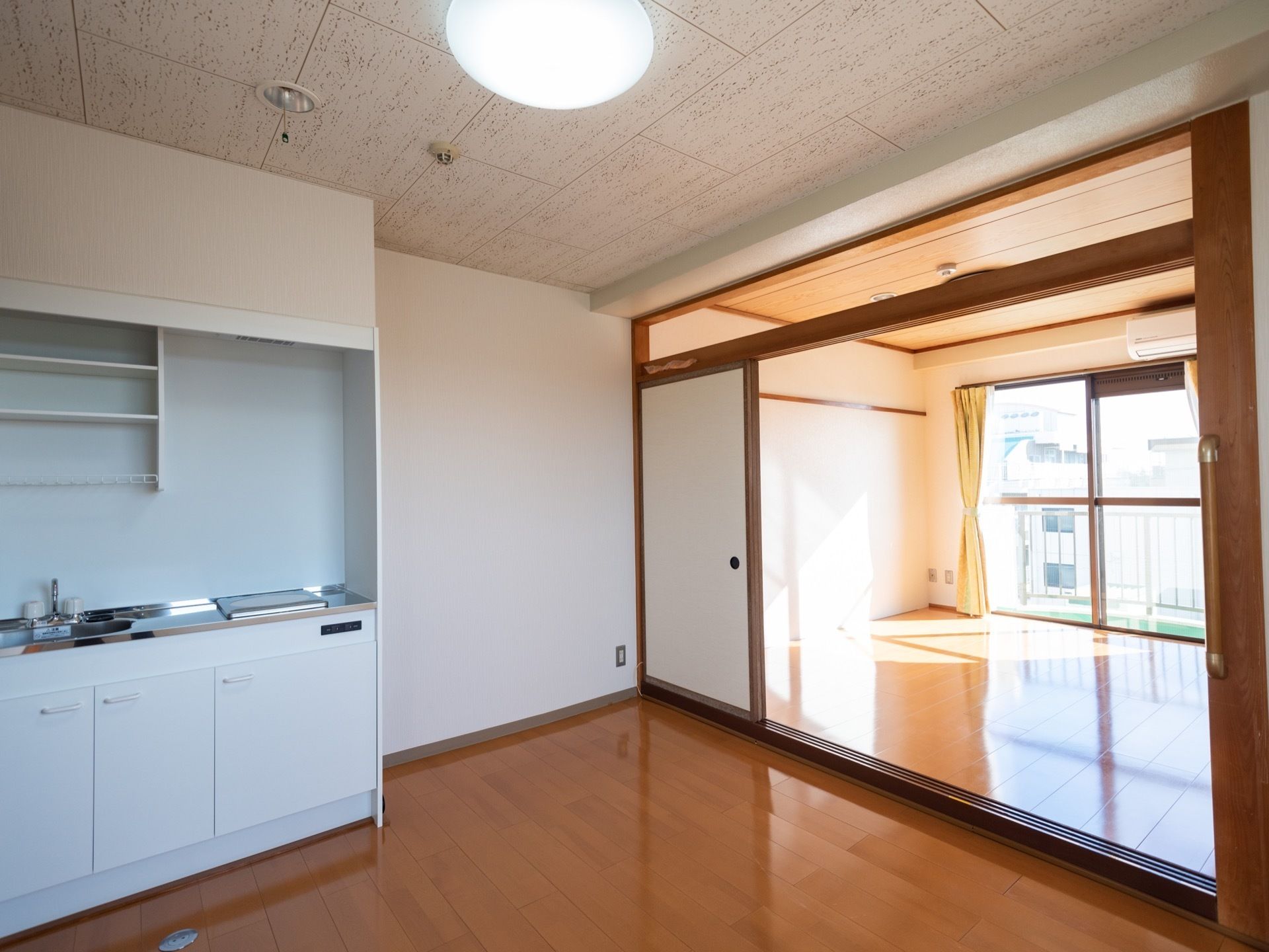 居室は二間続きで、フローリング床となっている。手前の部屋にキッチンが設置されている。奥の部屋には、広い掃き出し窓から陽光が差し込んでいる。
